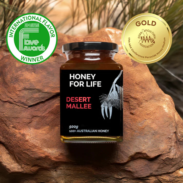 Glas med Honey For Life, Desert Mallee honing, foran en rød klippesten, og 2 vinderdiplomer, Australien