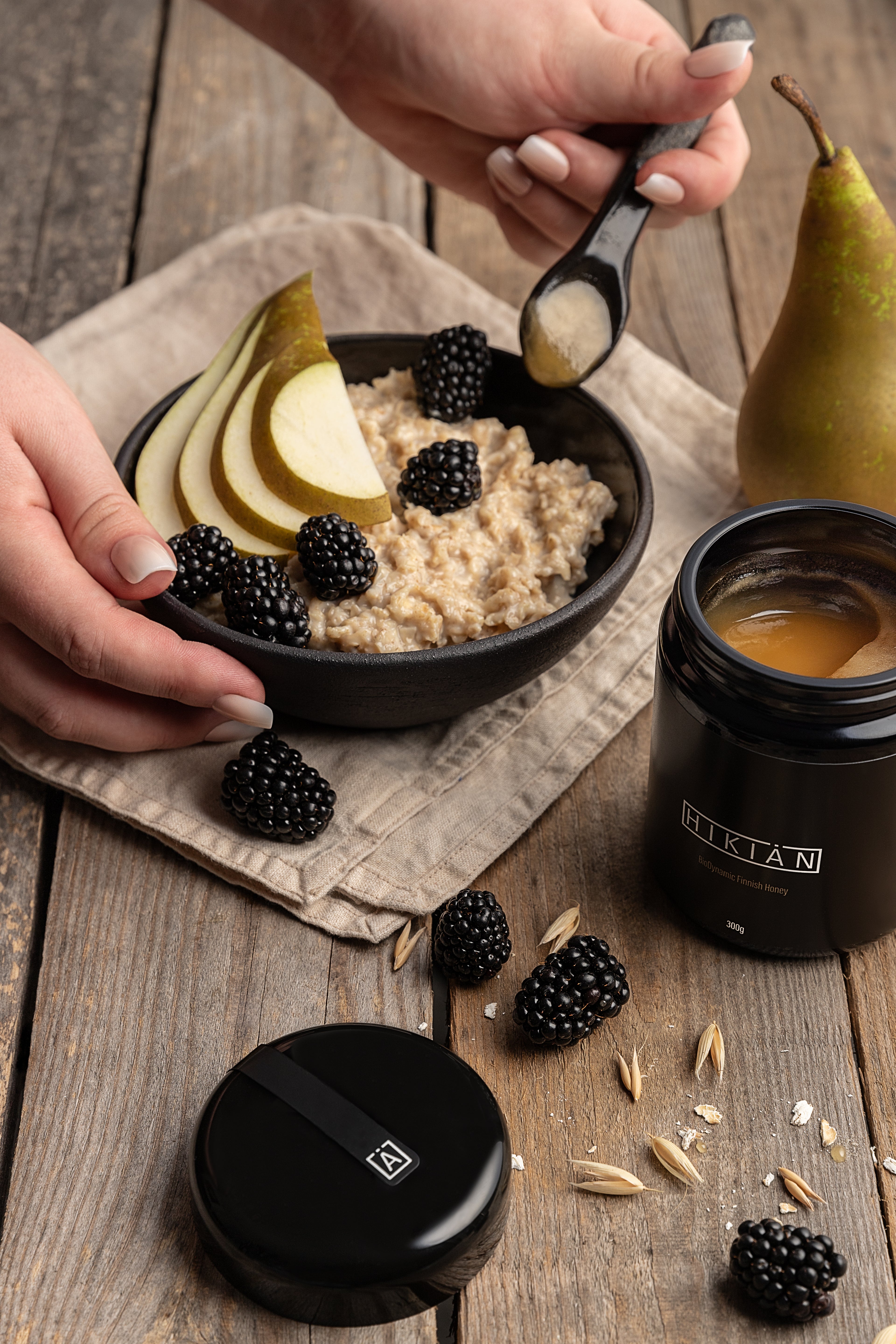 sjælden og exceptionel Hikiän – finsk honning i sin reneste form, i ekslusiv sort glas, på et bord med morgengrød med pærer og brombær. 